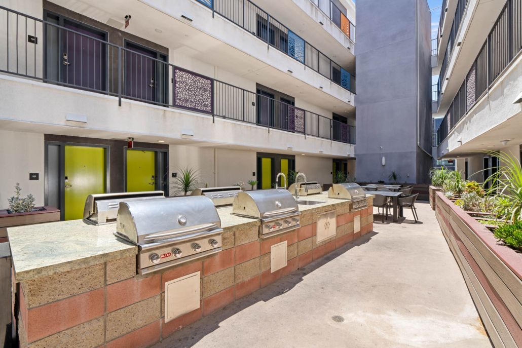 Apartment courtyard with outdoor grills, patio tables, and multi-story buildings on both sides