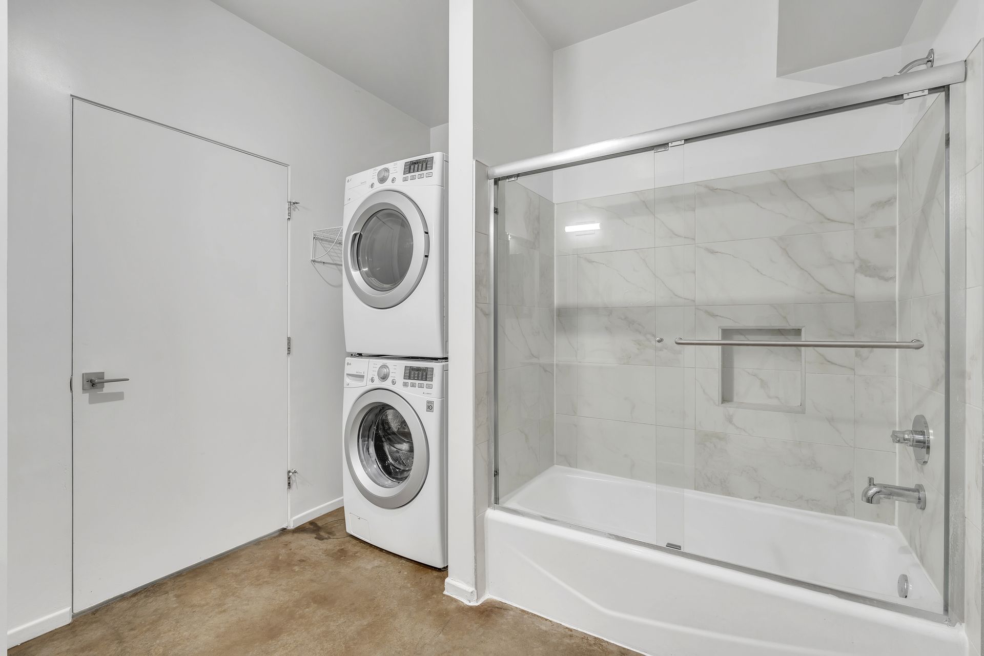 Bathroom with stacked washer/dryer, shower, white walls and door.