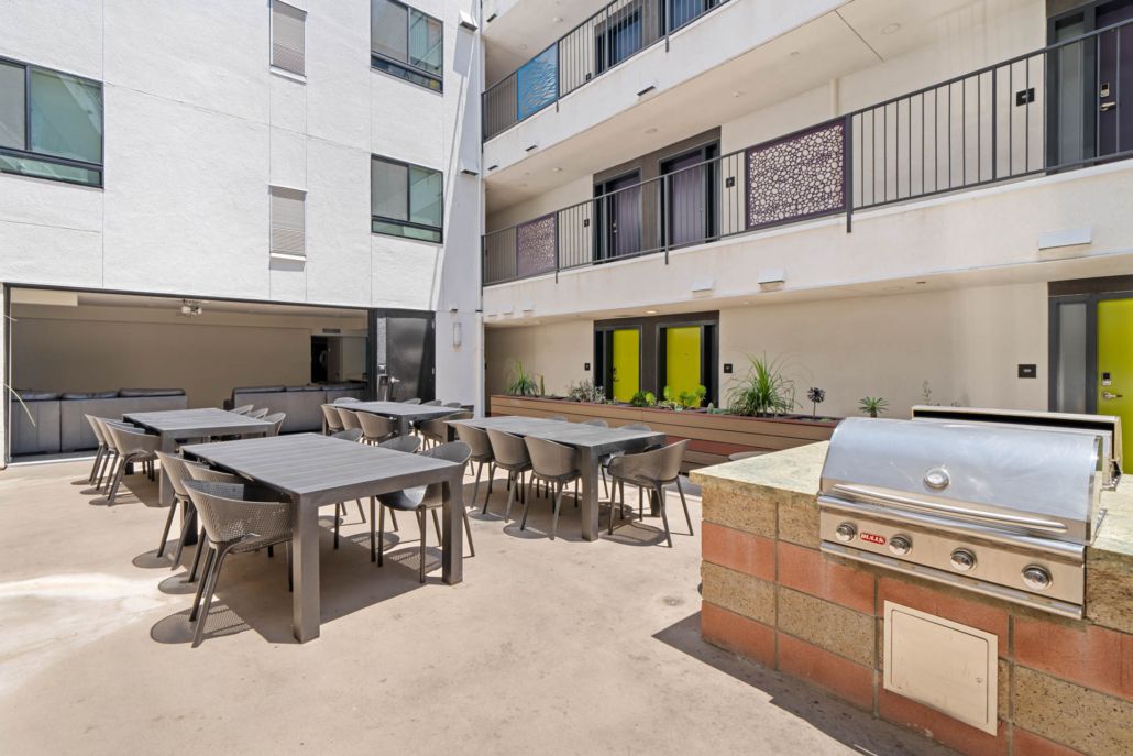Courtyard patio with tables and chairs beside a brick barbecue grill and apartment buildings