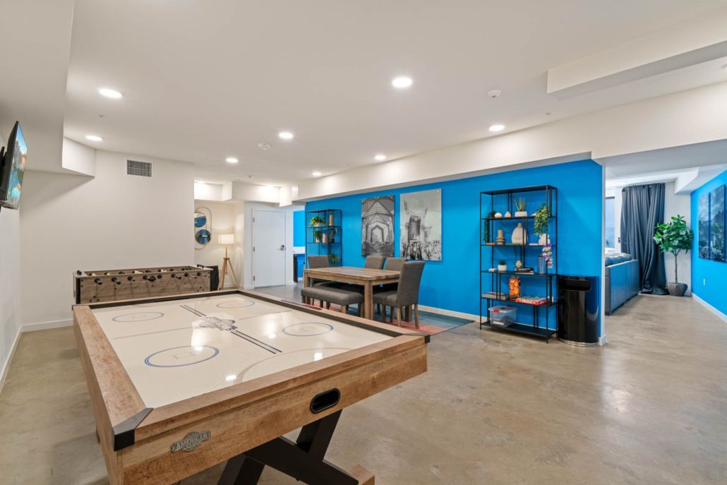 Modern game room with a shuffleboard table, blue accent wall, and dining area under recessed lights
