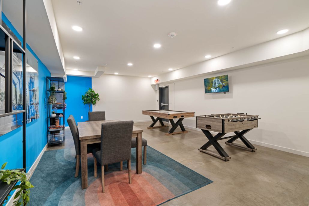 Bright game room with foosball tables, a dining table, blue accent wall, and carpeted play area.
