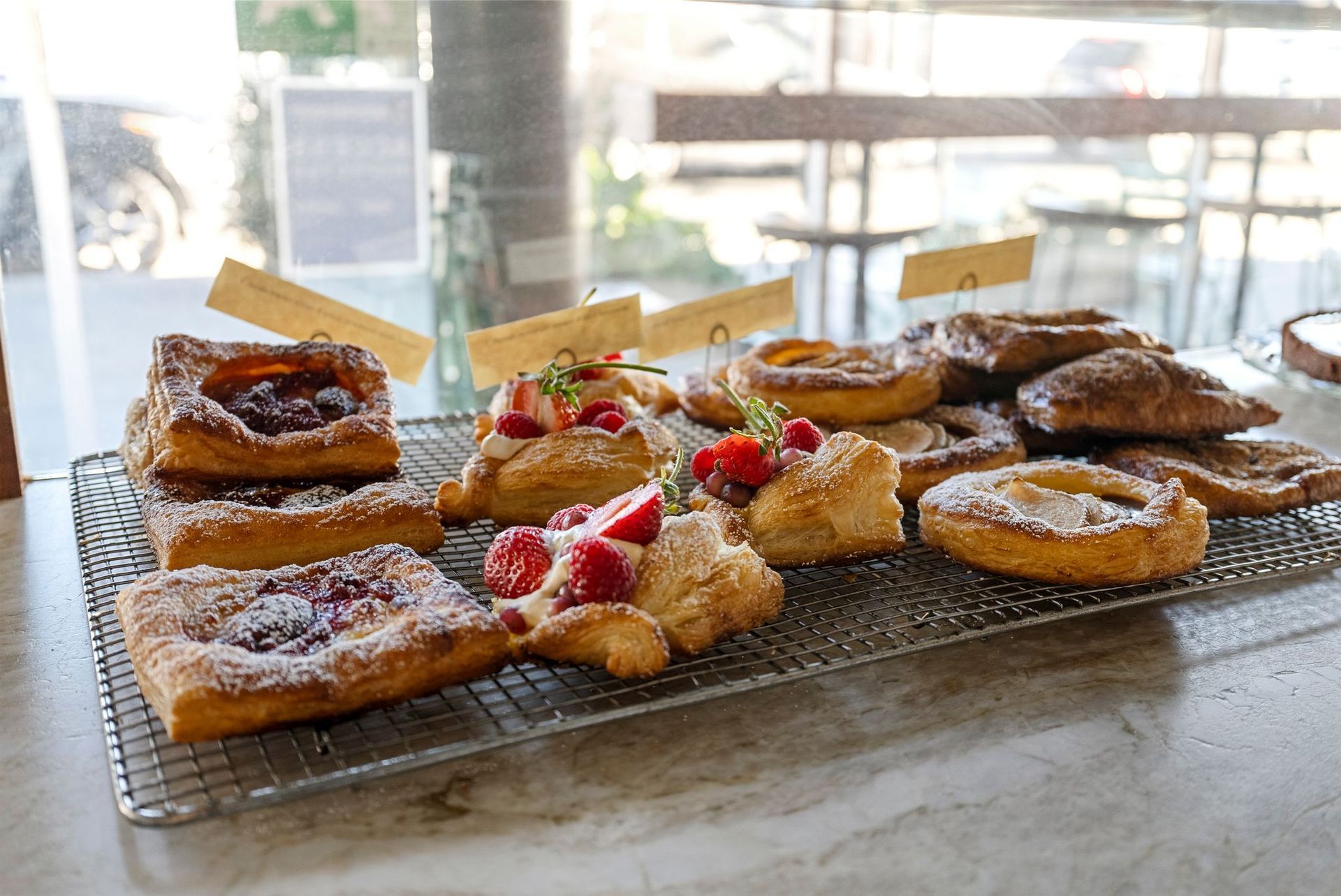 Pastries on a wire rack in front of a window. Some have berries and powdered sugar.