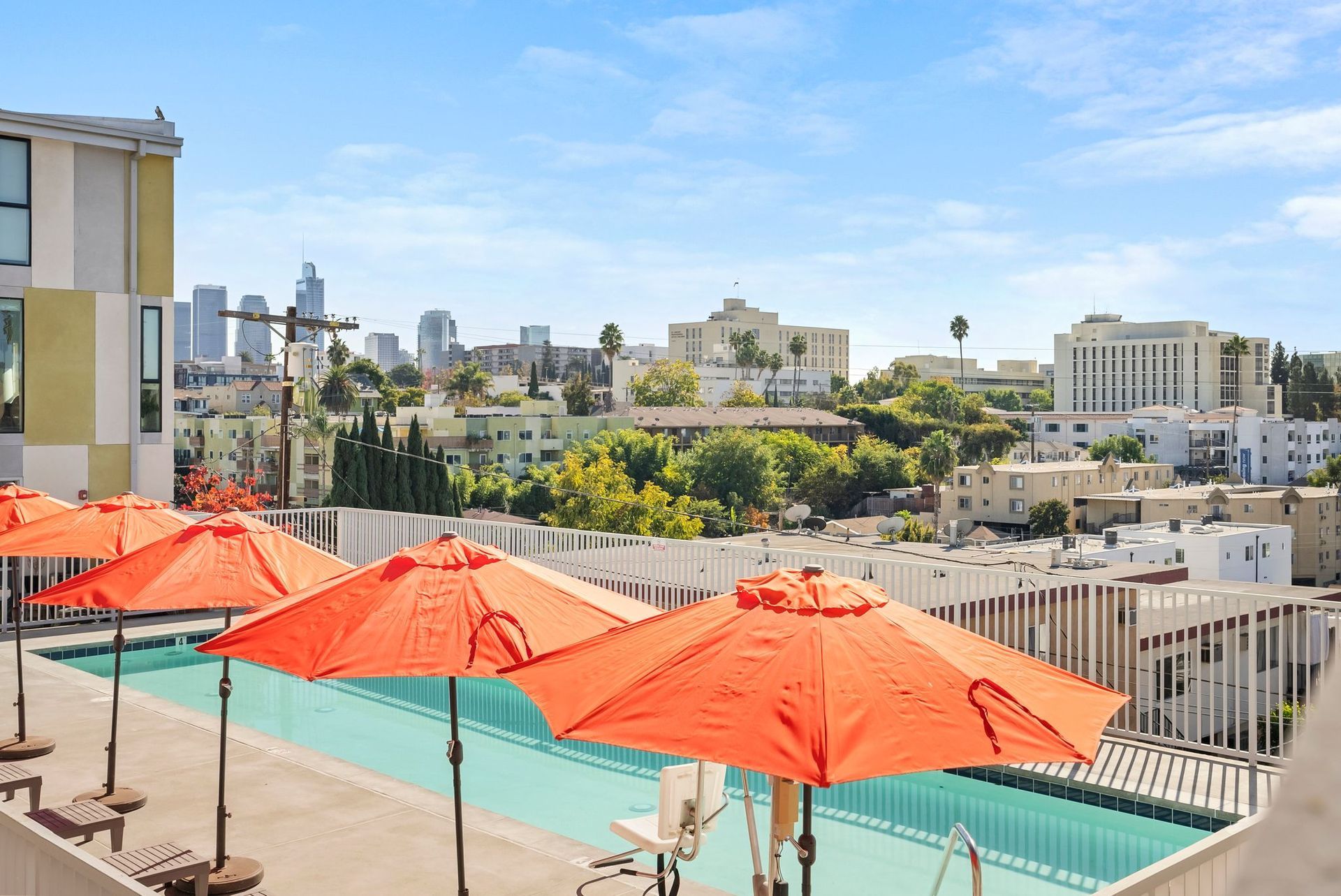 City skyline view with red patio umbrellas and a turquoise pool under a clear blue sky