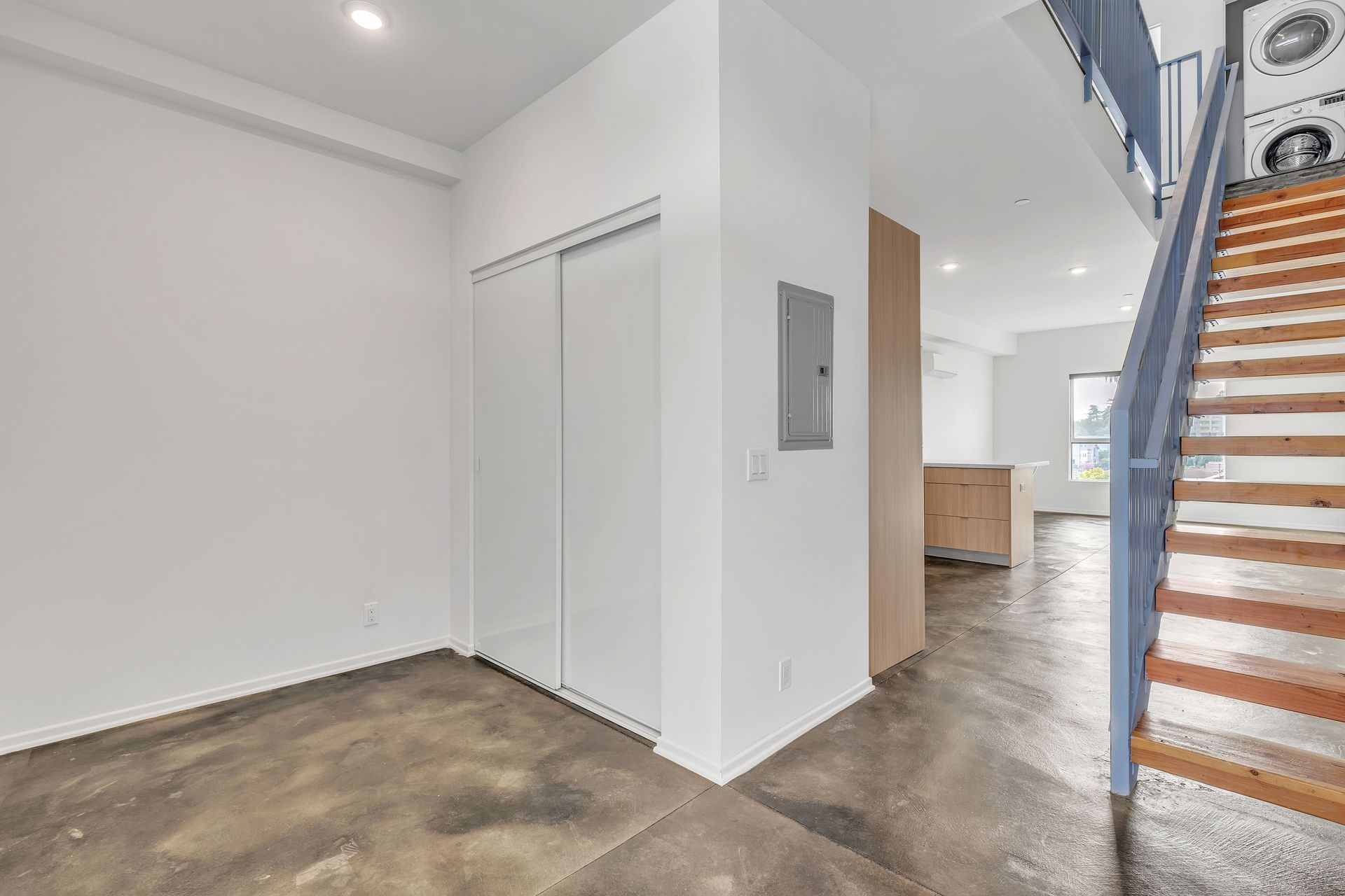 Interior view of a modern apartment with a staircase and concrete floors; a large closet on the left.
