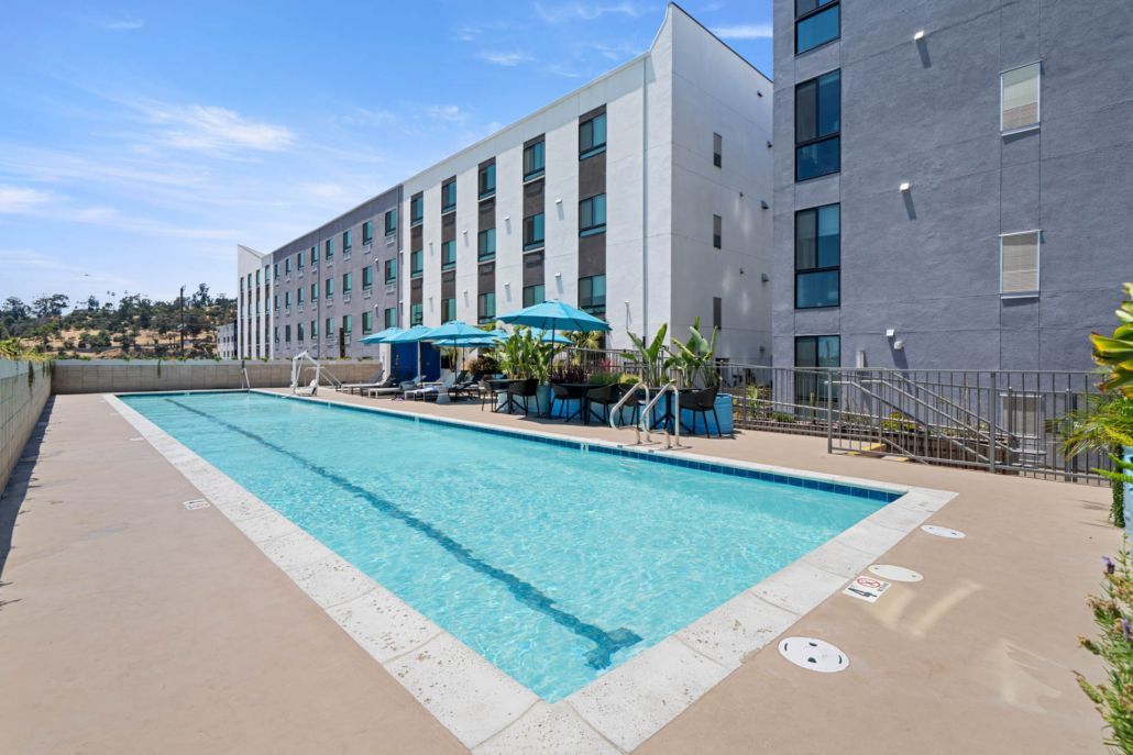 Outdoor hotel pool beside a modern building, with blue water and lounge chairs on the deck