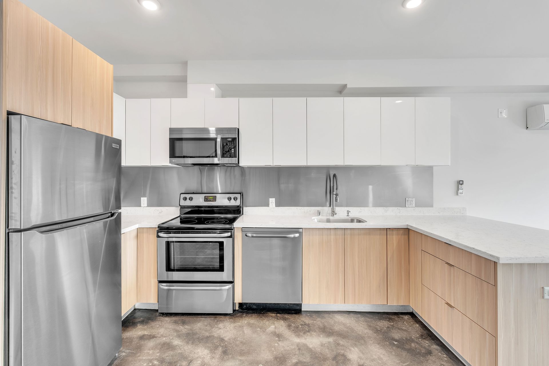Modern kitchen with stainless steel appliances, light wood cabinets, and white countertops.