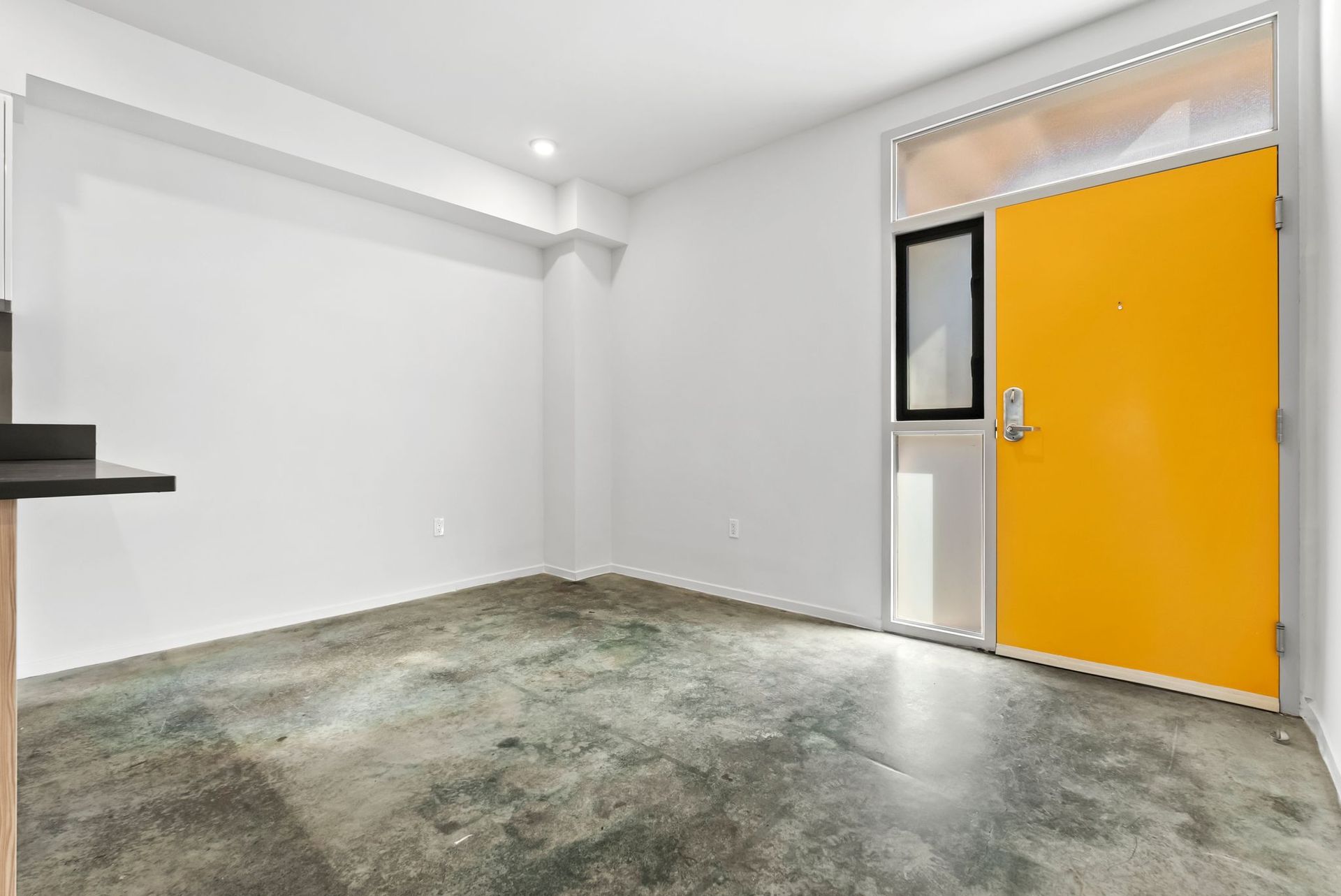 Empty white room with concrete floor and a bright yellow door on the right