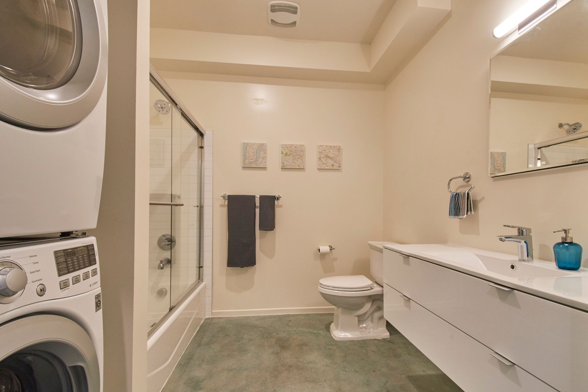 Bright modern bathroom with washer-dryer, glass shower, white vanity, toilet, and gray towels