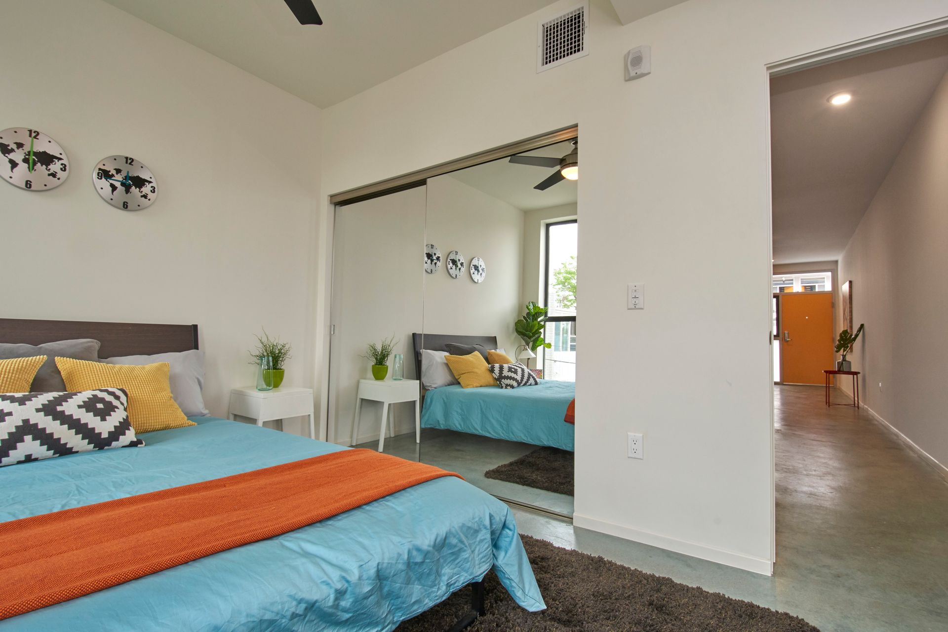 Bright bedroom with teal and orange bedding, mirrored closet, and hallway view into another room