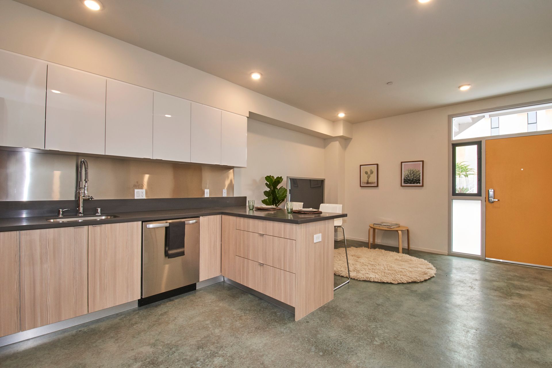 Modern kitchen with white cabinets, wood island, stainless appliances, and orange door to adjacent room