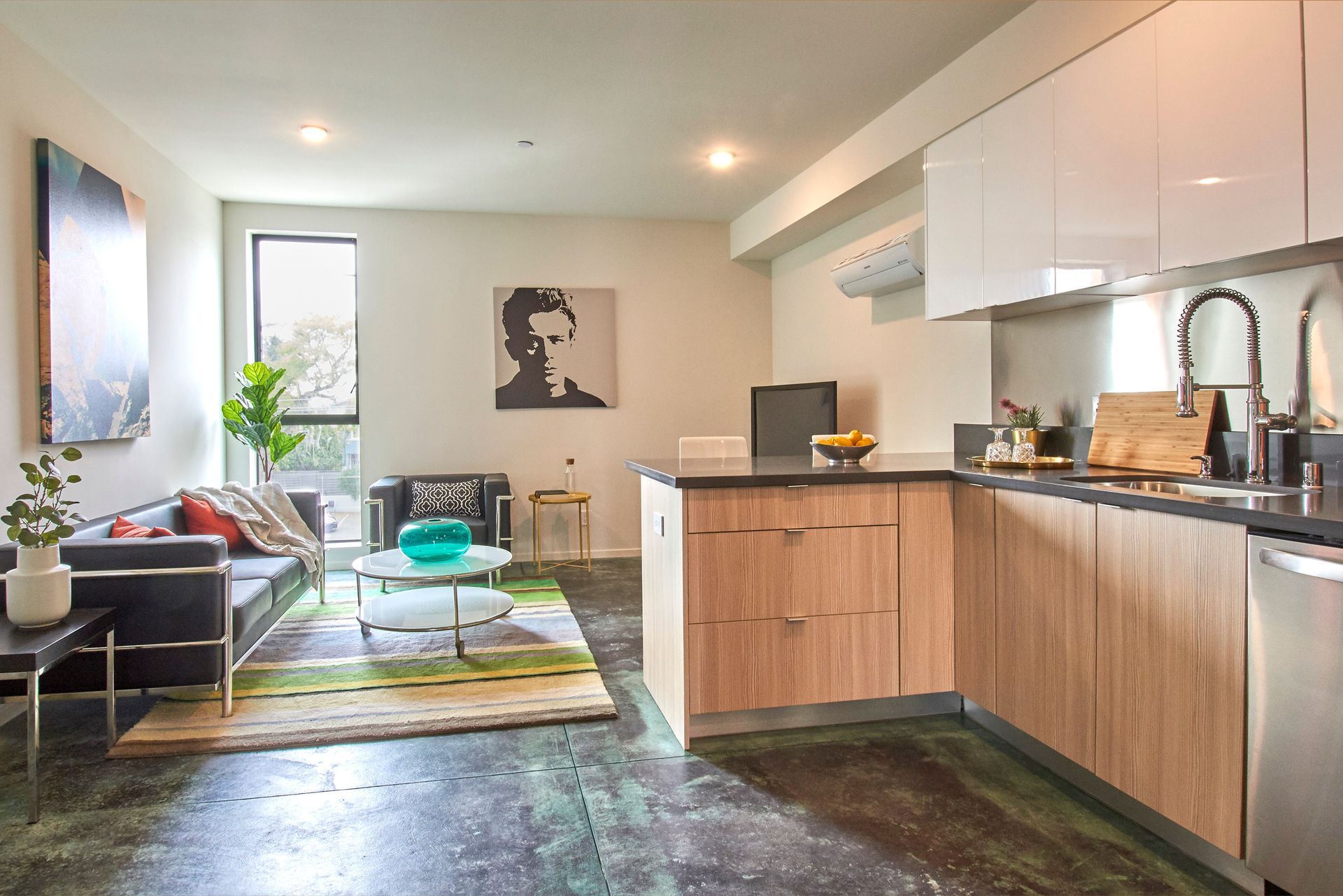 Bright open kitchen and living room with wood cabinets, sofa, rug, and large window.