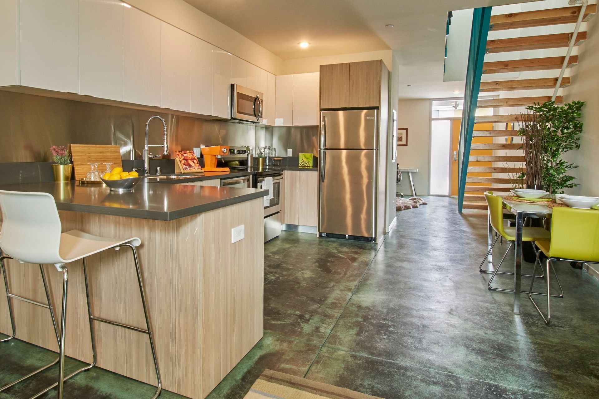 Modern kitchen with island, stainless steel fridge, and dining area beside a staircase
