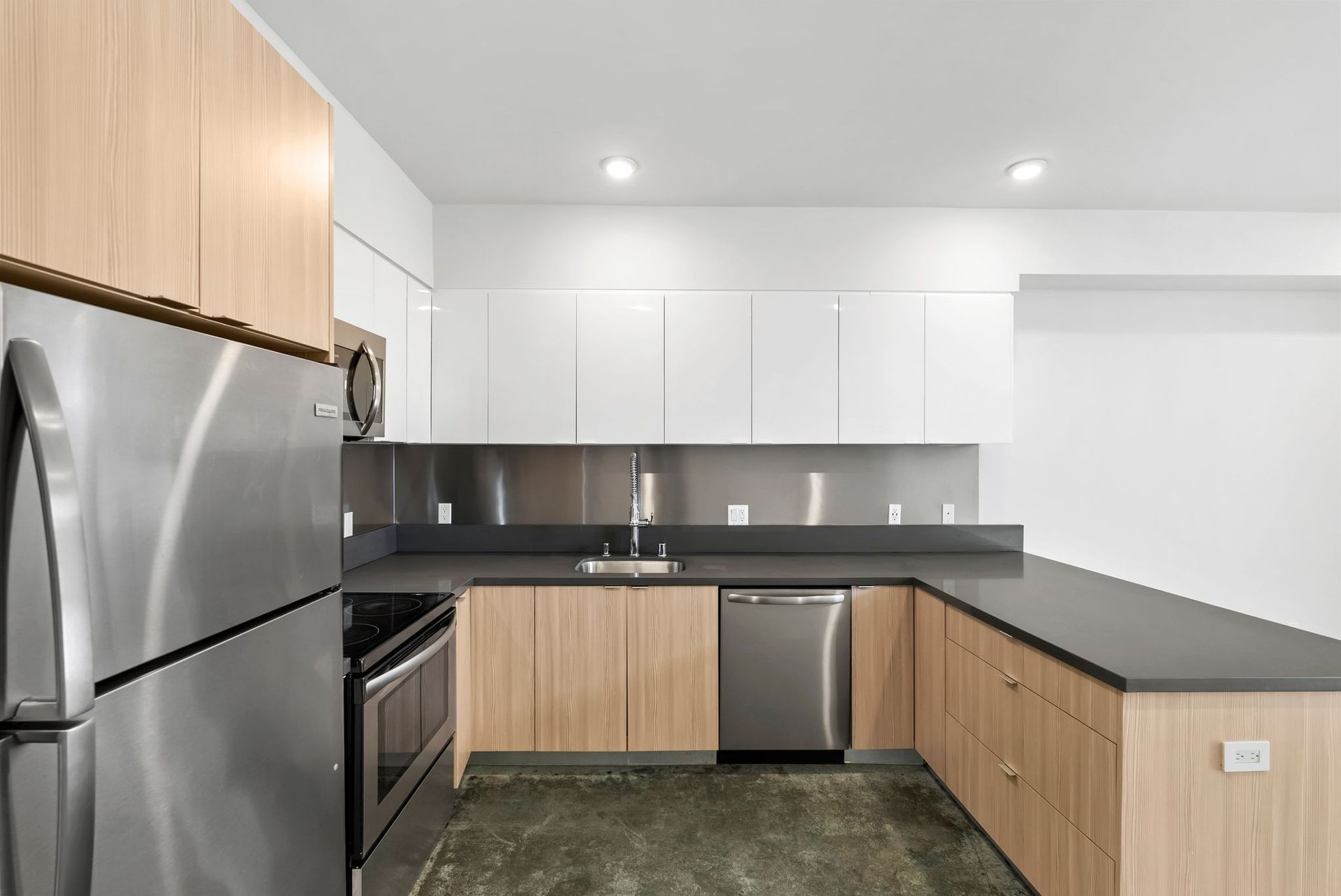 Modern kitchen with stainless steel appliances, white cabinets, wood accents, and dark countertops