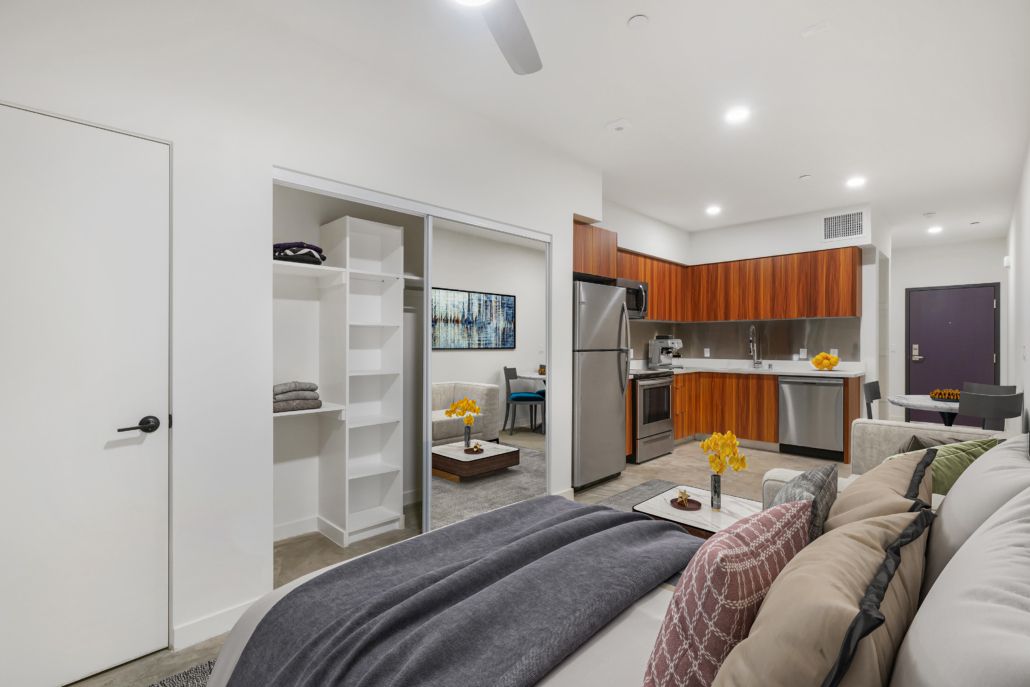 Modern living room with gray sofa, open kitchen, white shelving, and wall-mounted TV