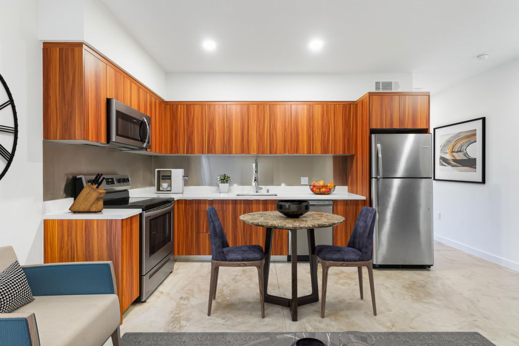 Modern kitchen and dining area with wood cabinets, stainless steel appliances, and a small table with stools