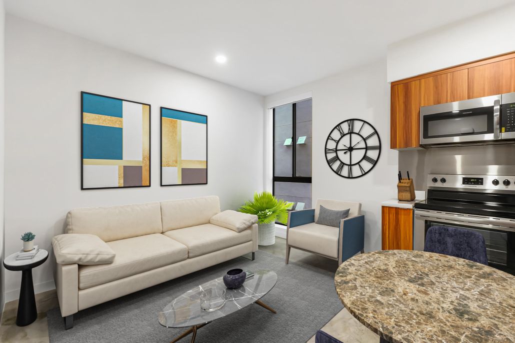 Bright modern living room with beige sofa, wall art, clock, and open kitchen with wood cabinets.