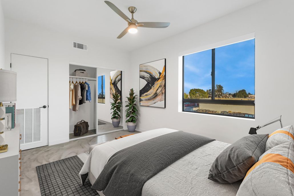 Bright bedroom with gray bed, large window, ceiling fan, and open closet view