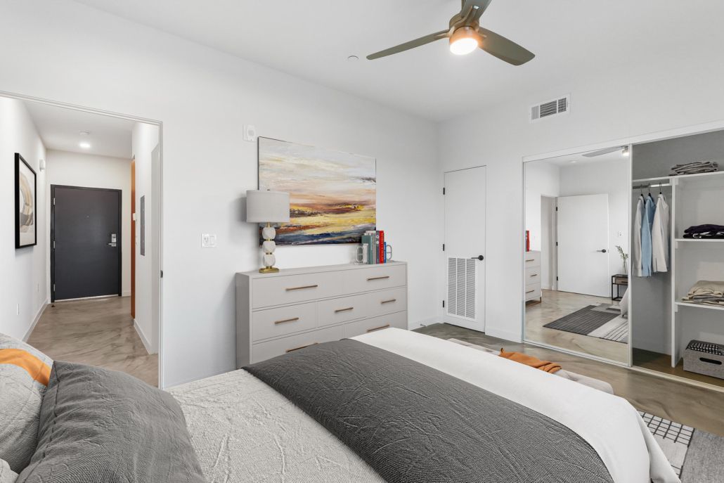 Bright bedroom with gray bed, dresser, ceiling fan, mirror, and closet doors open