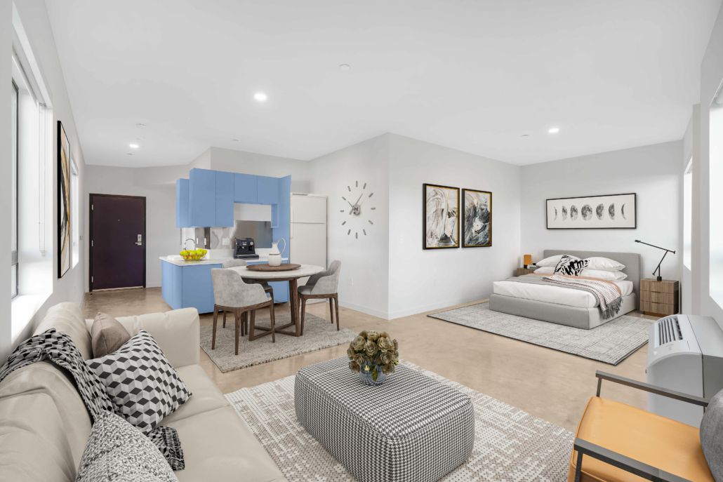 Open-plan studio with beige sofa, dining table, and bed in a bright modern apartment
