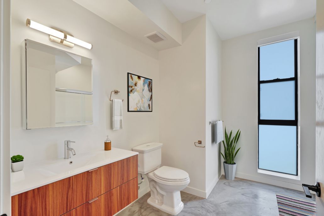 Bright modern bathroom with wood vanity, sink, toilet, mirror, and frosted window.