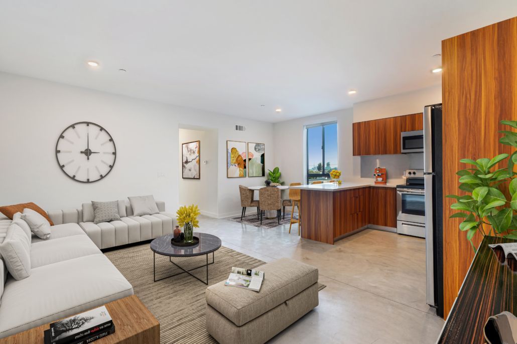 Bright open-plan living room with gray sofa, round wall clock, and kitchen island with wood cabinets
