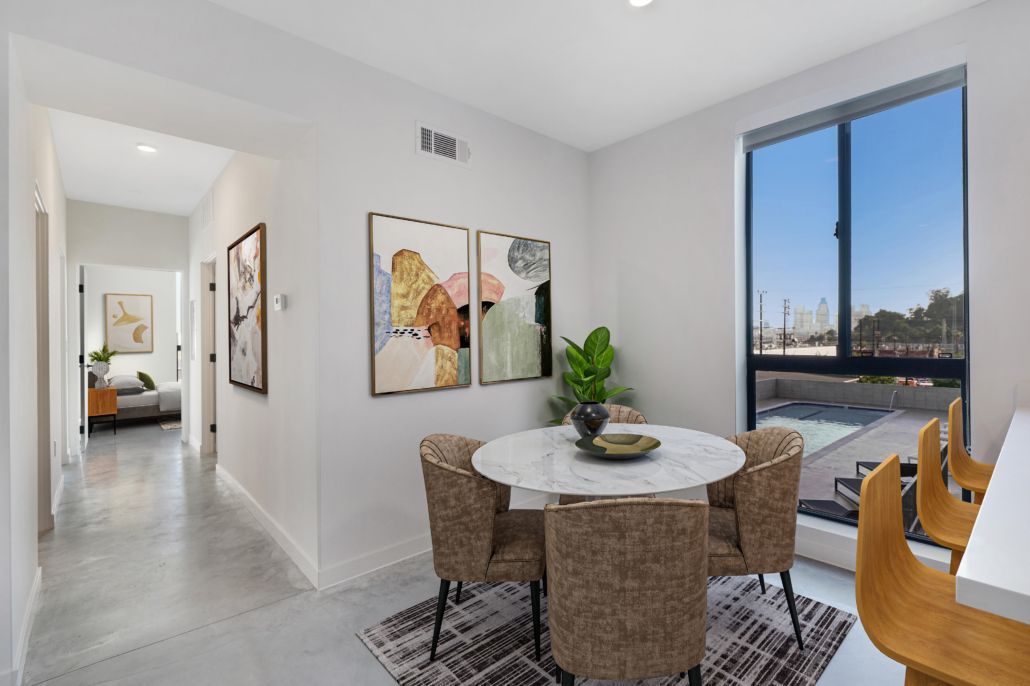 Bright dining nook with round table, woven chairs, wall art, and a large window overlooking the city.