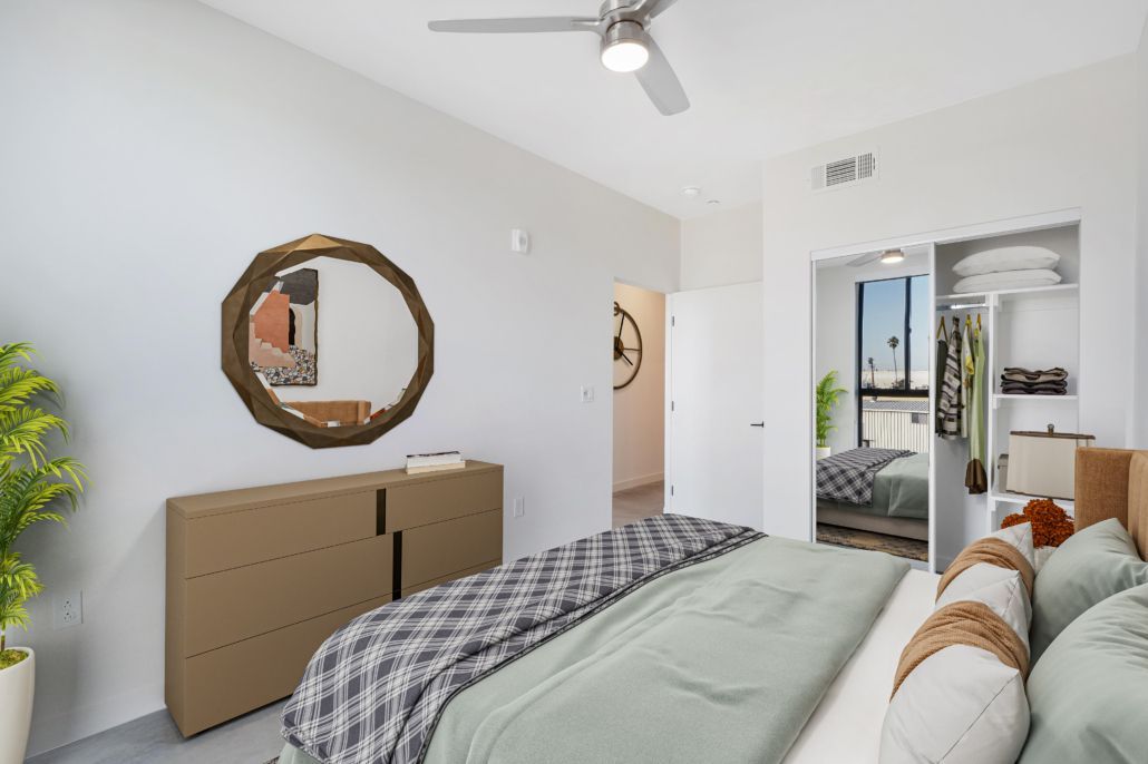Bright bedroom with bed, dresser, round mirror, ceiling fan, and open doorway to a bathroom
