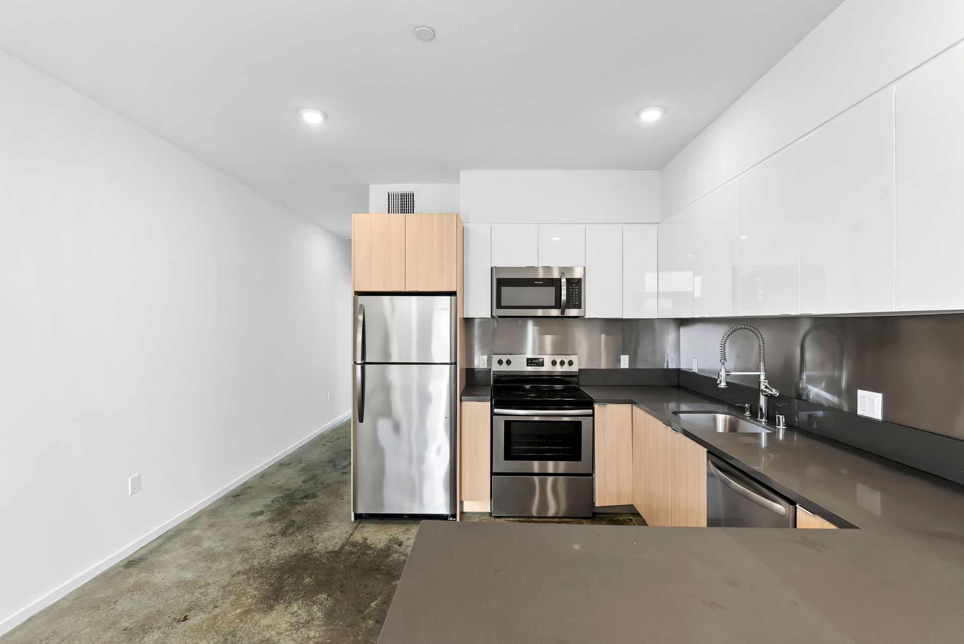 Modern kitchen with stainless steel appliances, white cabinets, black counters, and a small island.