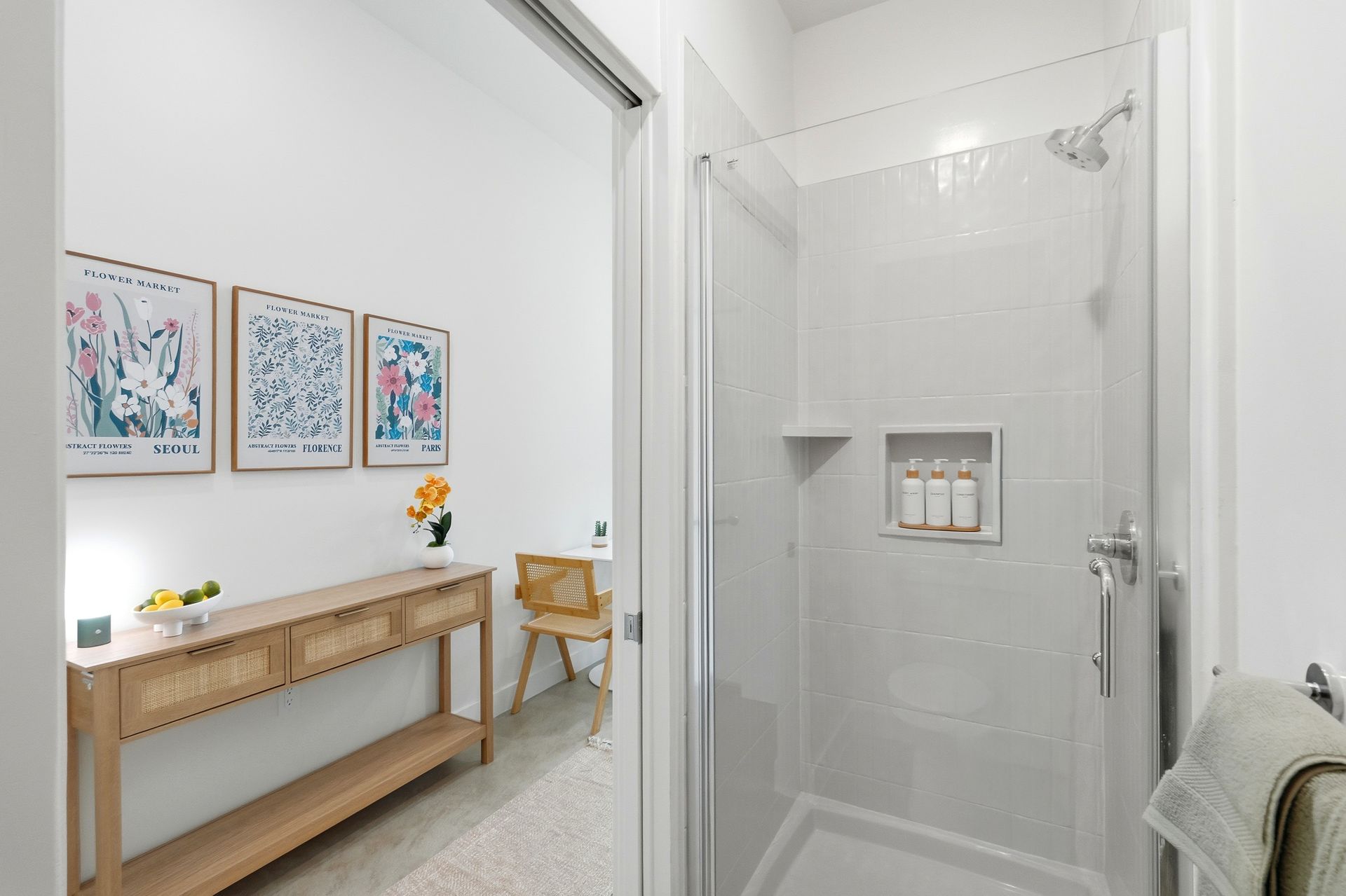 White bathroom with glass shower door, and an entryway with wall art and console table.