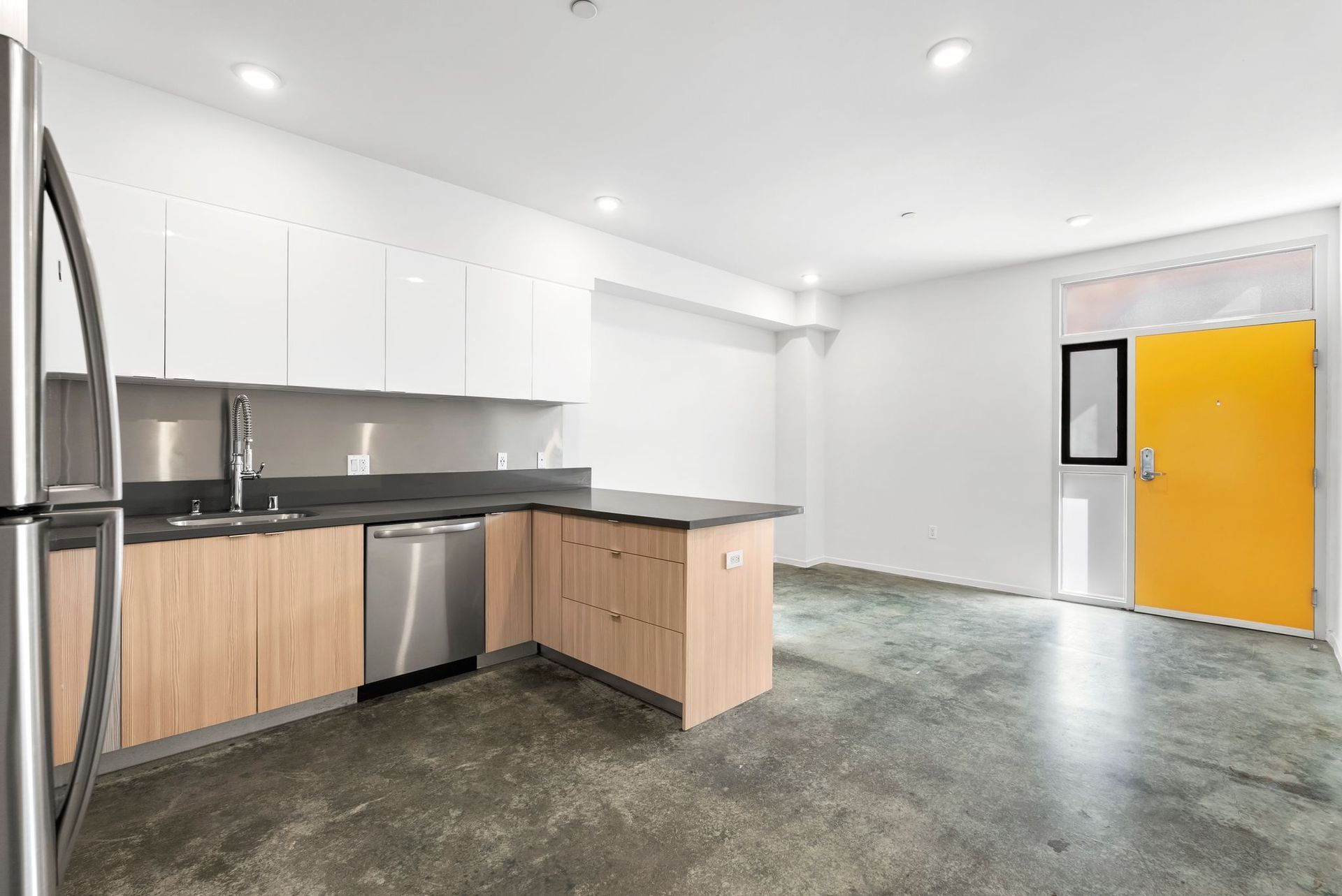 Modern kitchen with white cabinets, wood lower cabinets, gray counters, stainless appliances, and a bright yellow door