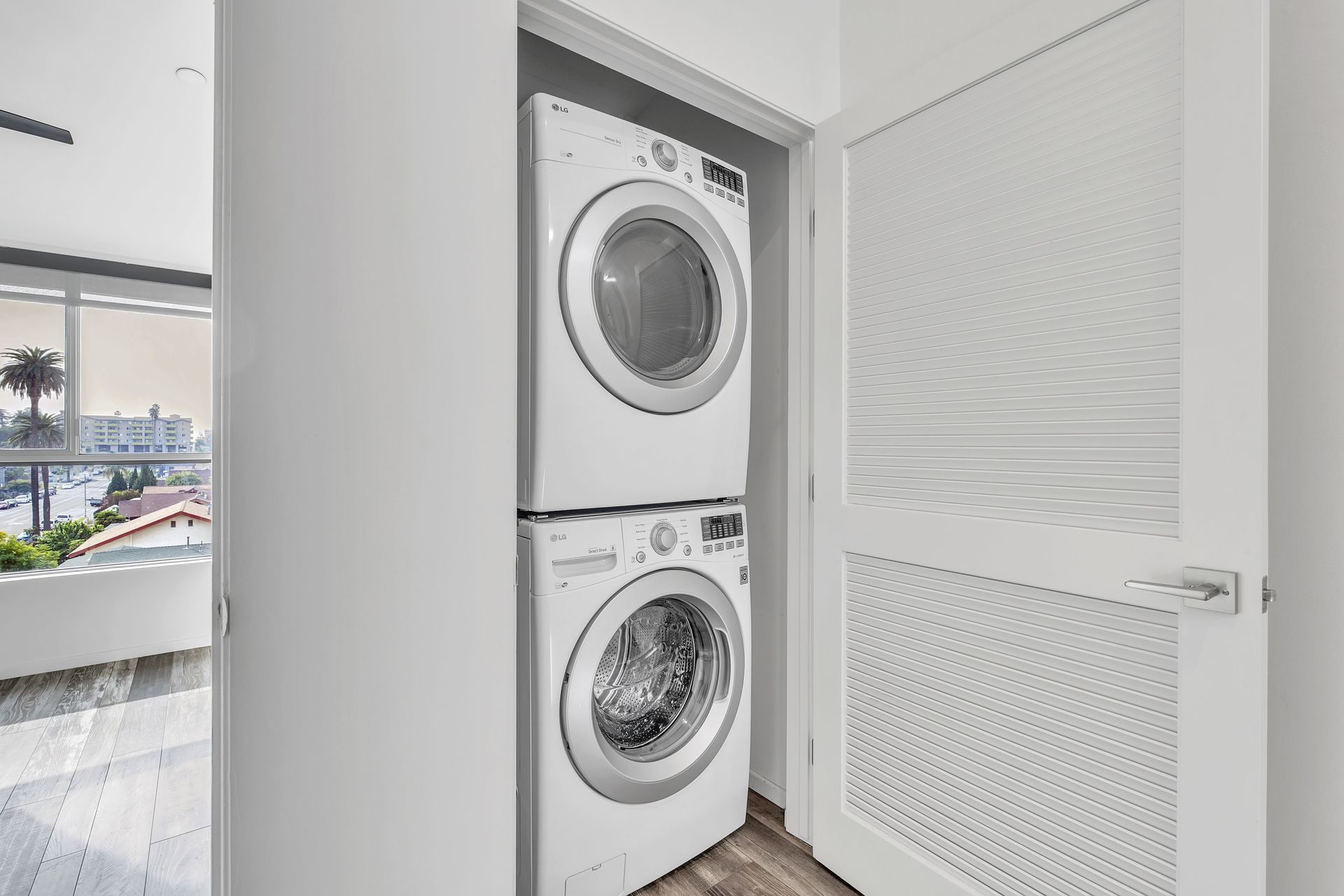 Stacked white washer and dryer in a white closet with a partially open, textured white door.