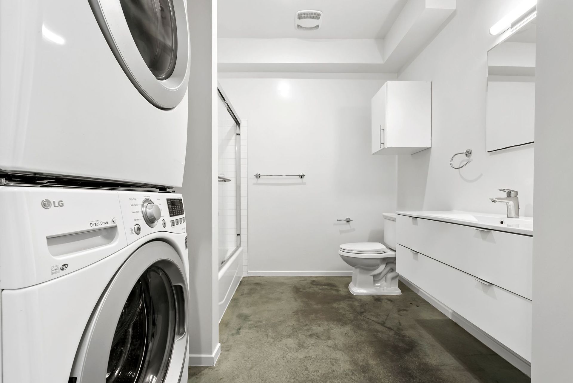 Modern white laundry room with stacked washer-dryer, vanity sink, toilet, and green rug