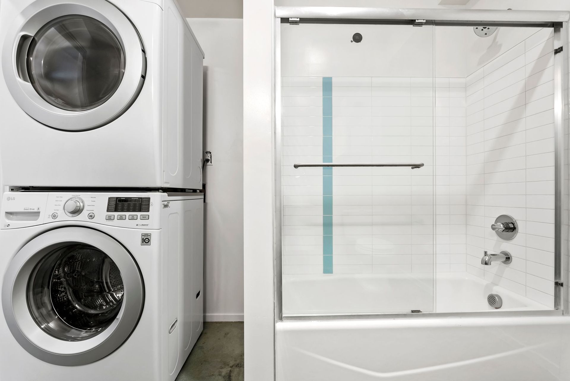 Stacked washer and dryer beside a white shower stall with glass door and chrome fixtures