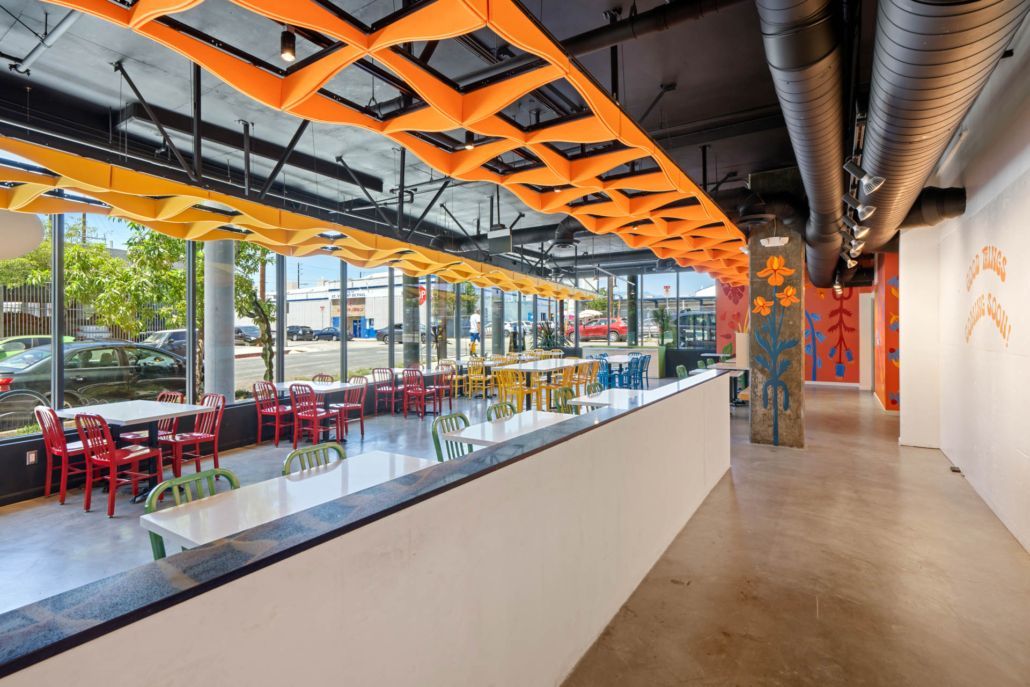 Modern indoor café with orange ceiling panels, red chairs, and a long counter by large windows