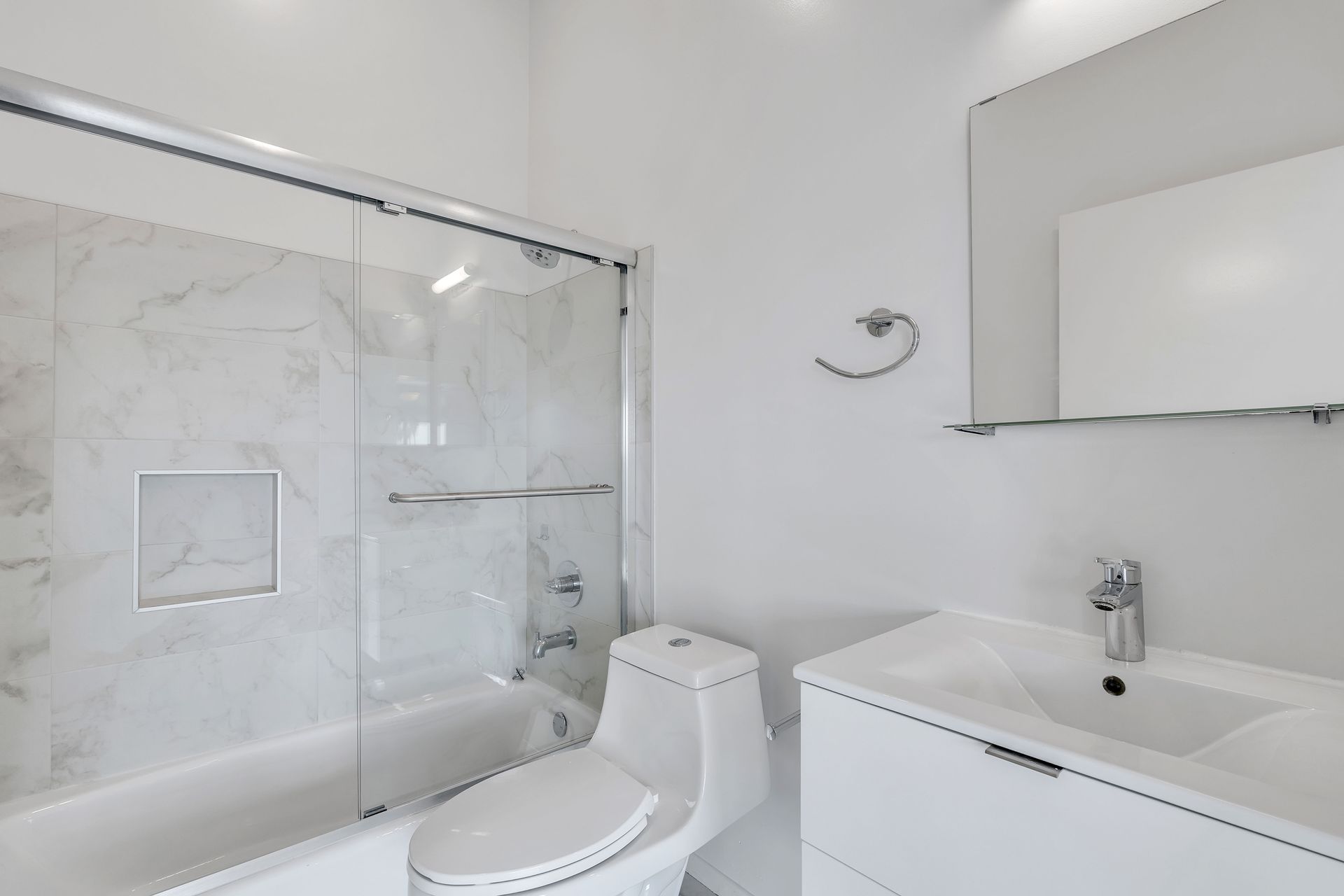 White bathroom with marble-look shower, white toilet, vanity, and mirror.