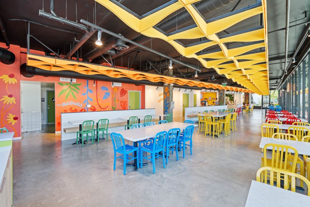 Colorful cafeteria with rows of yellow, blue, and green chairs under a bright geometric ceiling