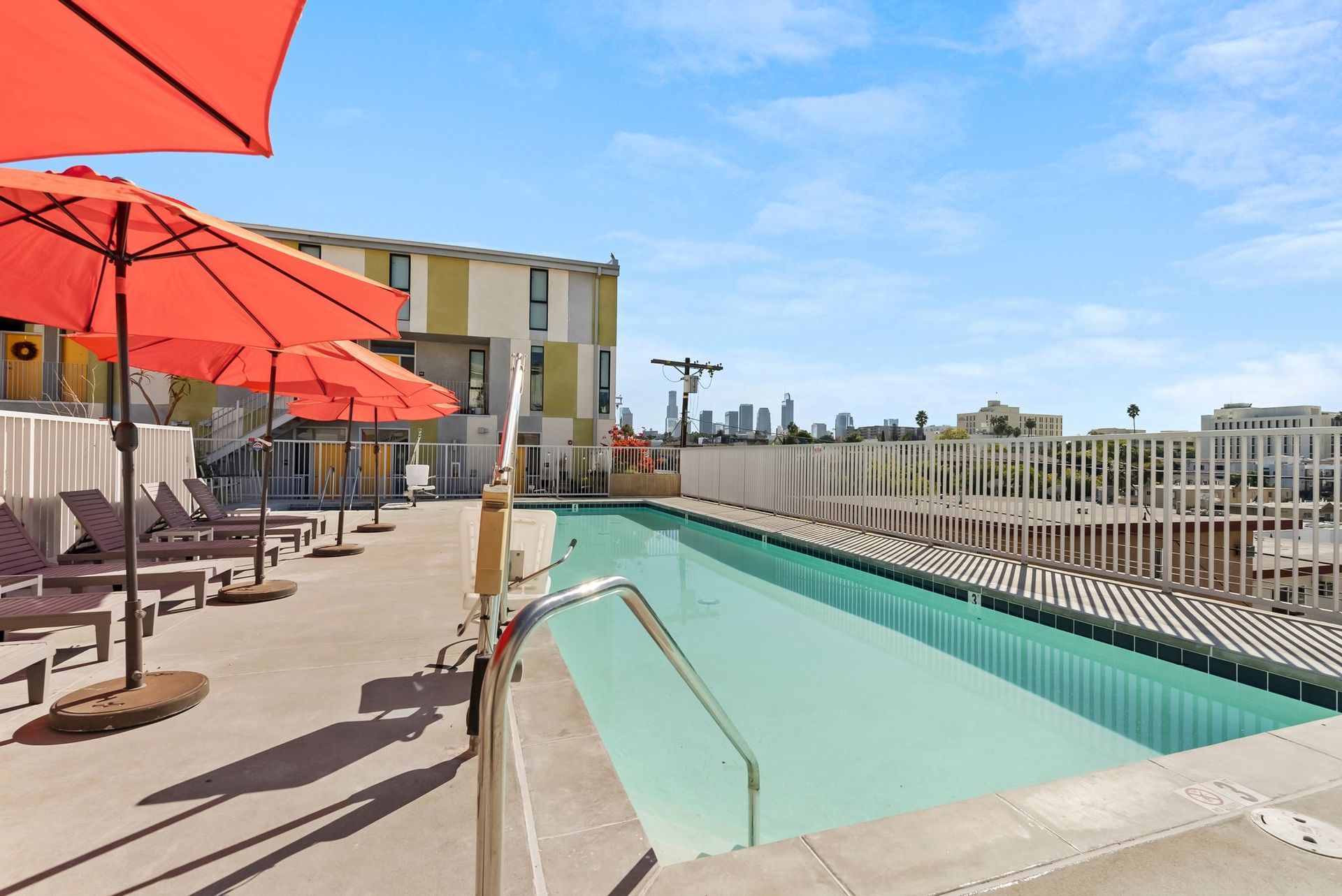 Rooftop pool with orange umbrellas and lounge chairs under a clear blue sky