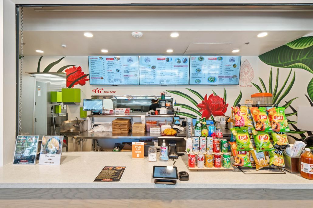 Bright café counter with pastries, drinks, menu screens, and colorful snacks behind the register