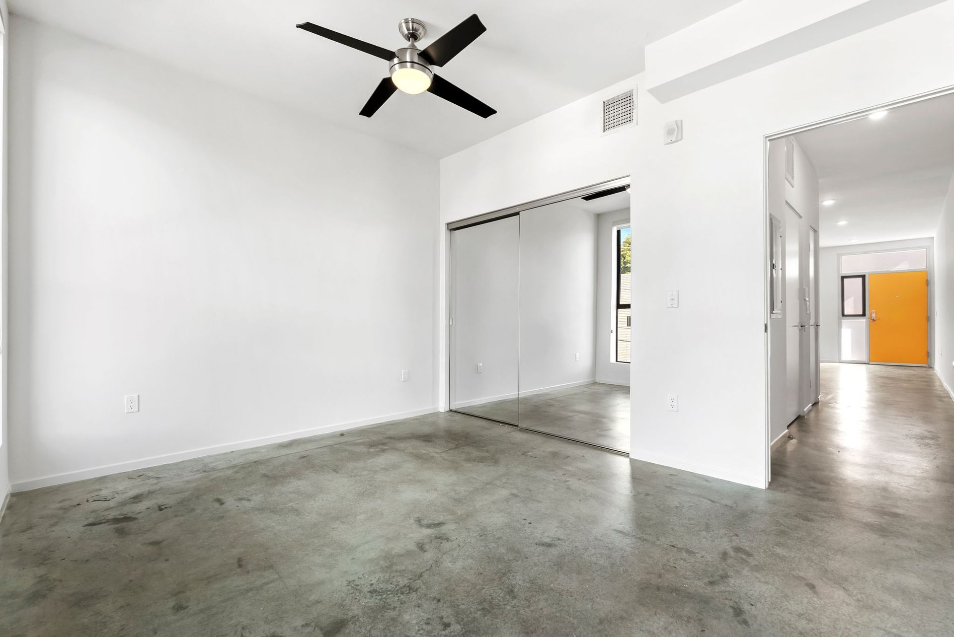 Empty white room with concrete floor, ceiling fan, and doorways leading to other rooms.