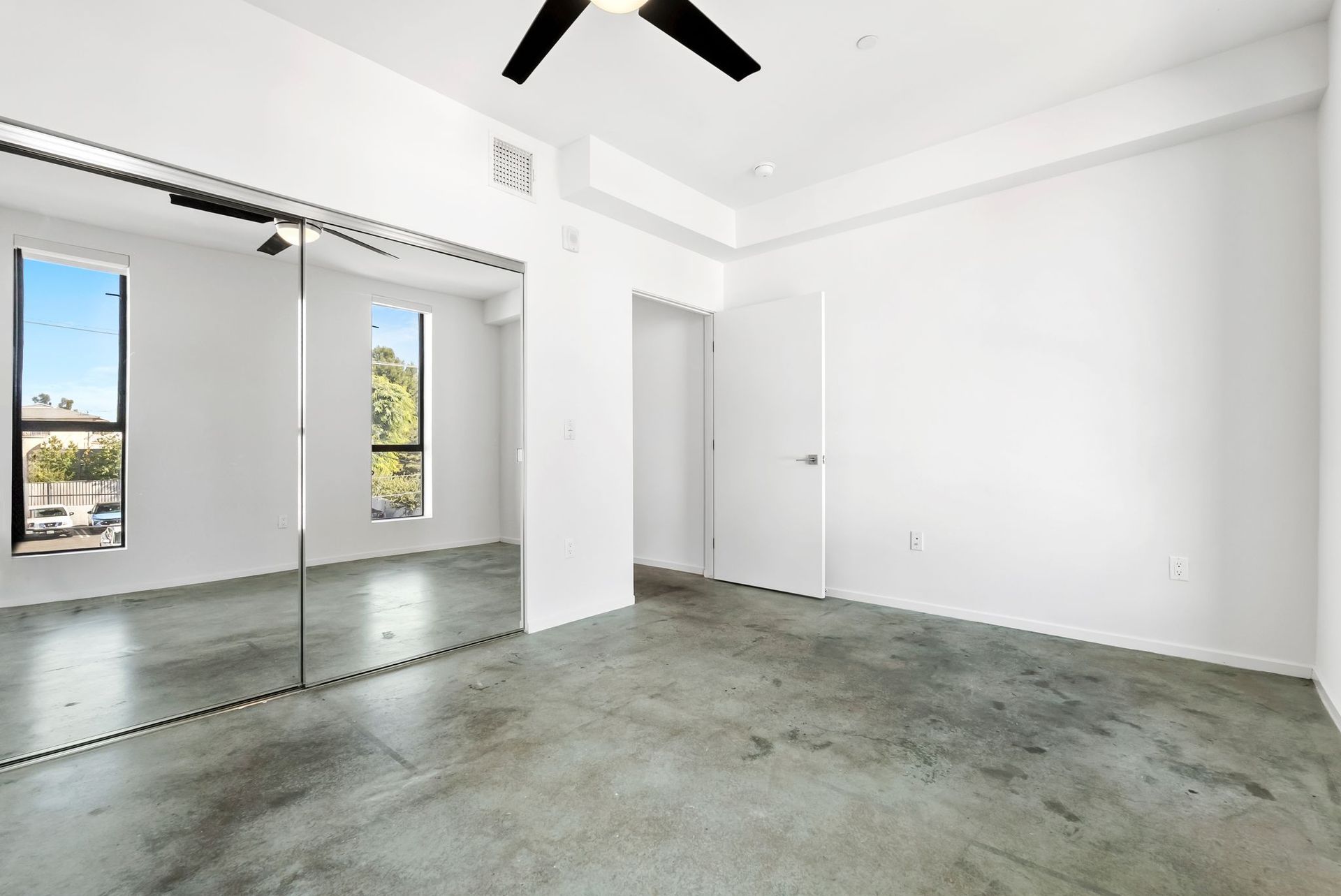 Empty modern room with white walls, mirrored closet doors, and polished concrete floor