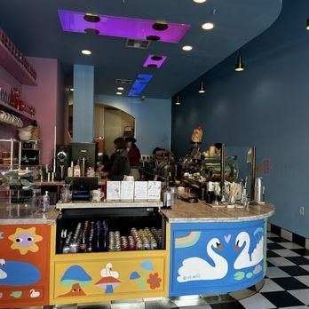 Colorful cafe interior with counter, swans, and customers near coffee machines.