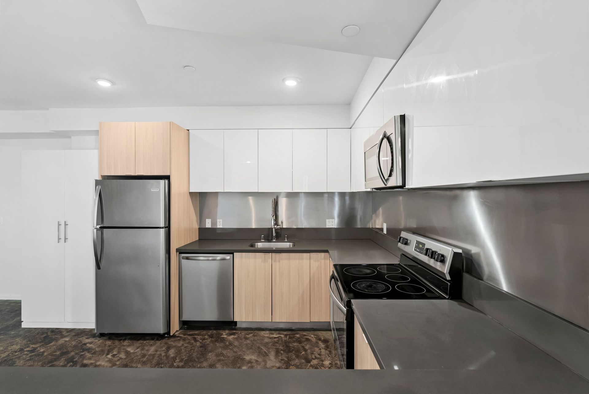 Modern kitchen with stainless steel fridge, white cabinets, black countertops, and tiled backsplash.