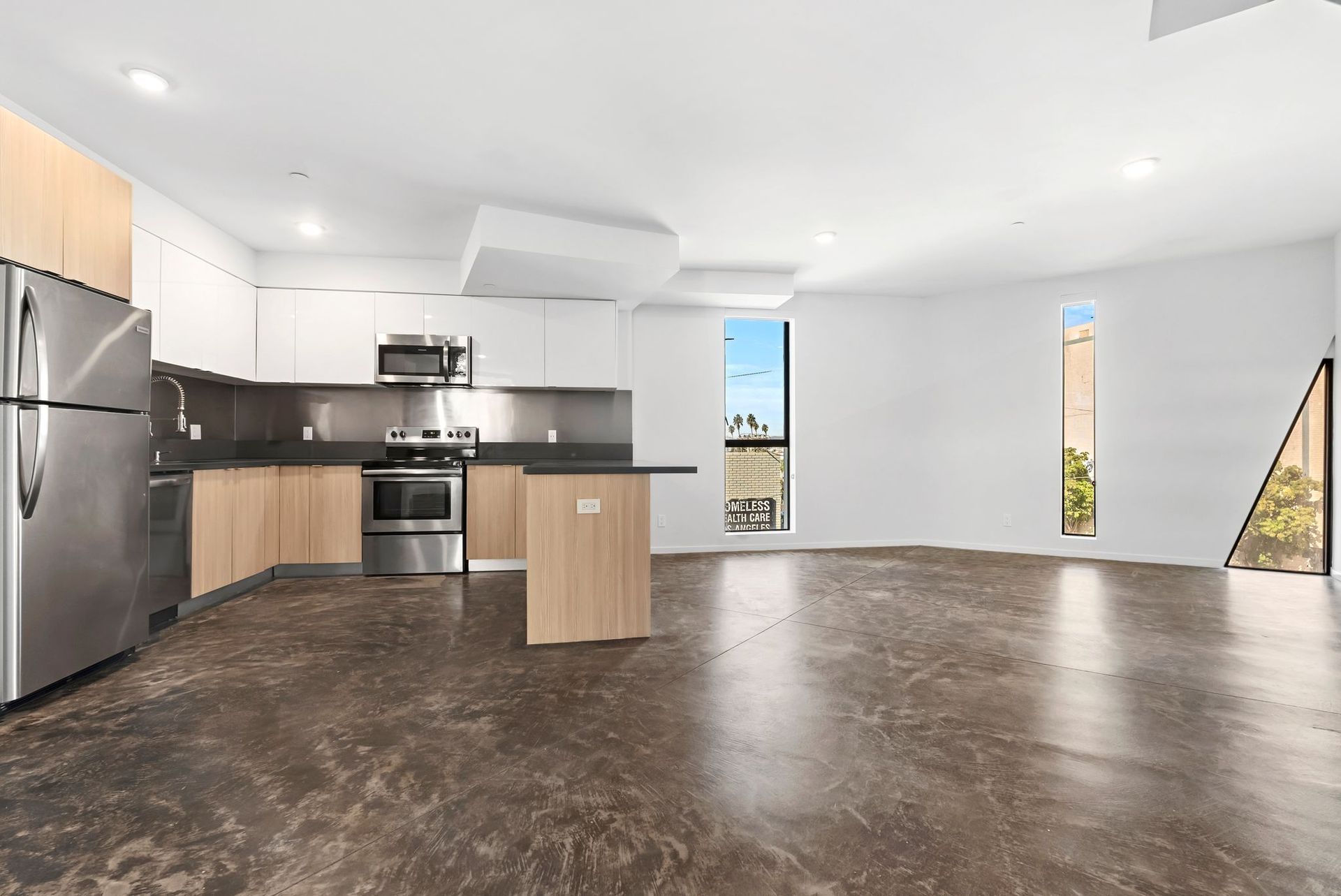 Modern open-plan kitchen and living area with dark floors, stainless appliances, and tall narrow windows.