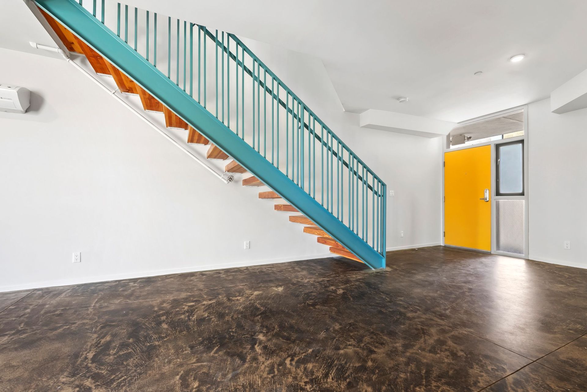 Empty room with dark floor, white walls, and a teal staircase beside a bright yellow door.
