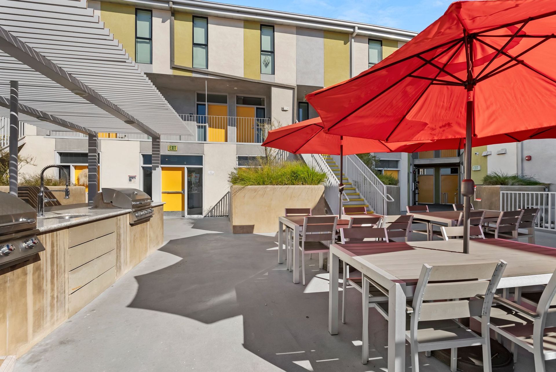Outdoor patio with red umbrellas, white tables, and a modern building in the background