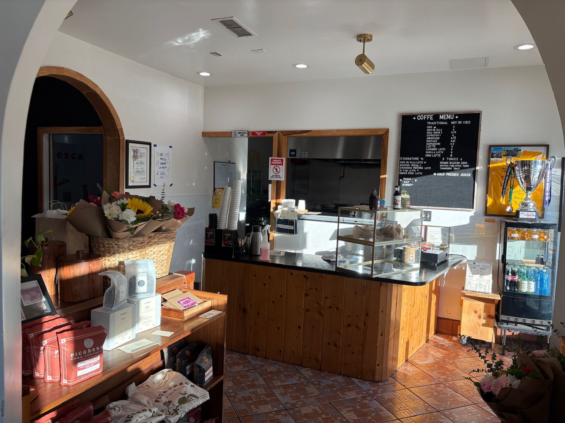 Interior of a cafe with a counter, baked goods, and products for sale. Sunlight illuminates the space.
