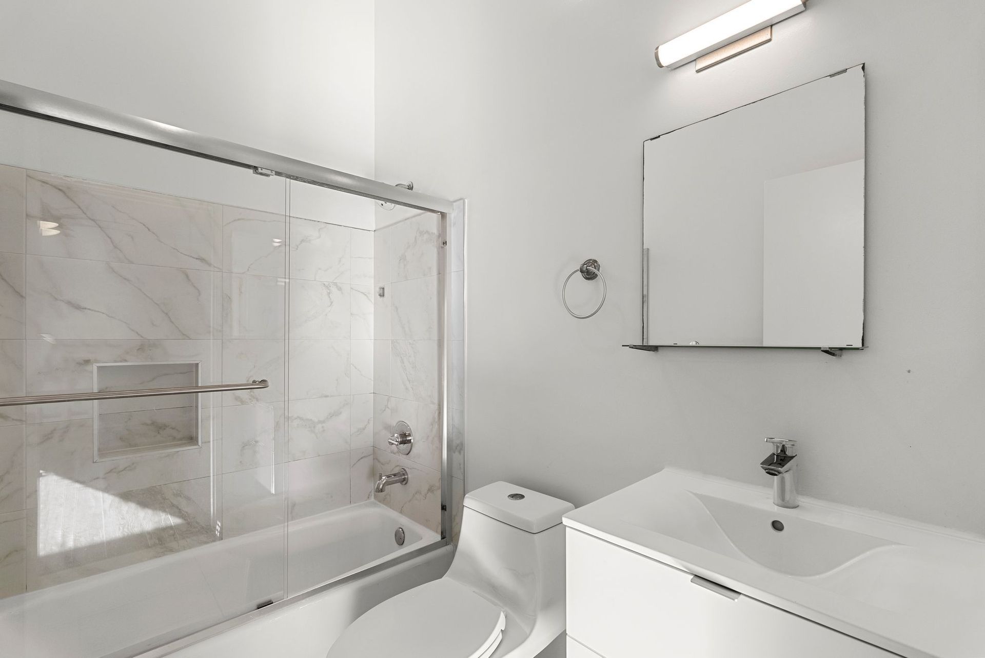 White bathroom with a shower, toilet, and sink. A mirror is above the sink, and a light is above the mirror.