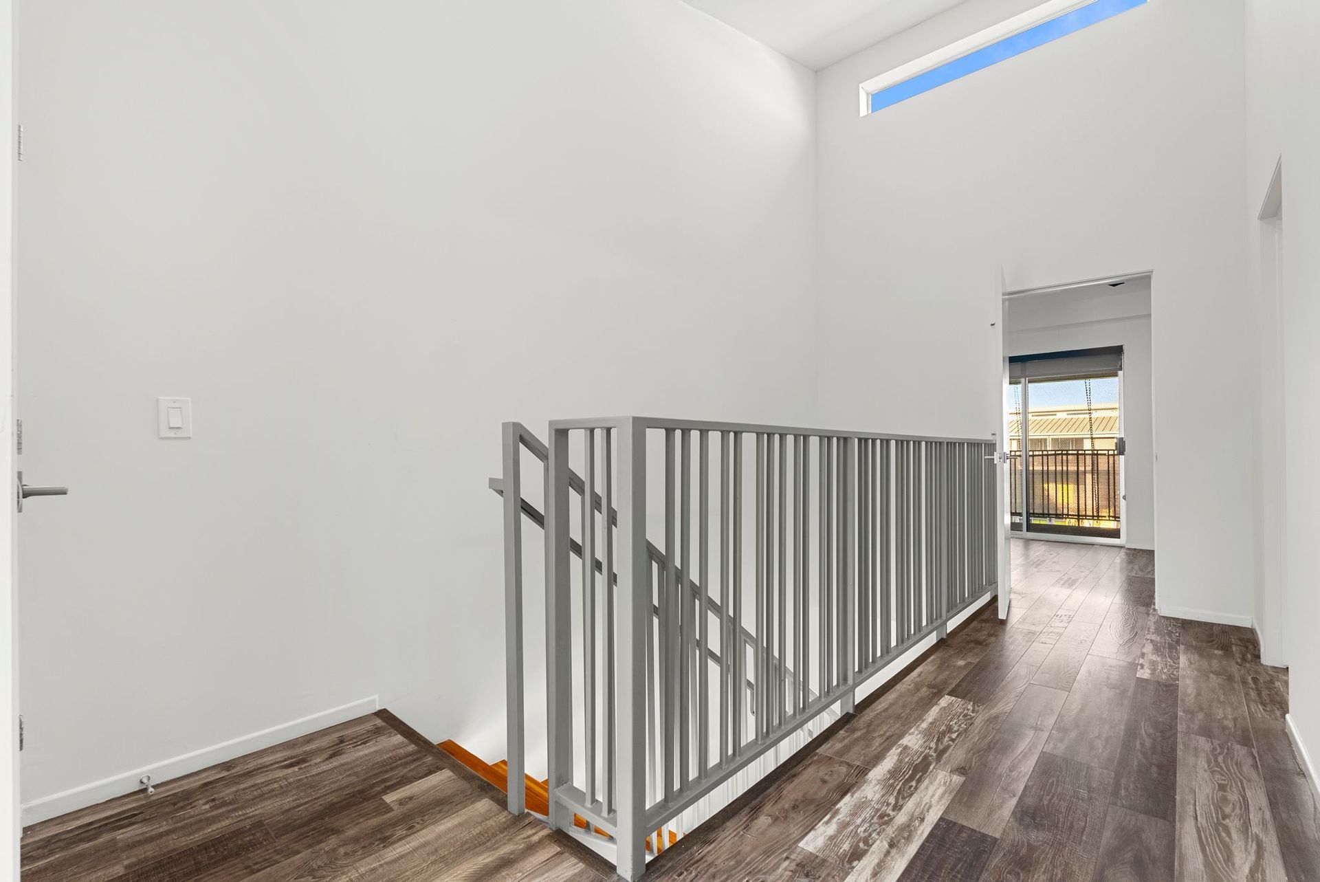 Interior hallway with wooden floor, white walls, and a metal railing.
