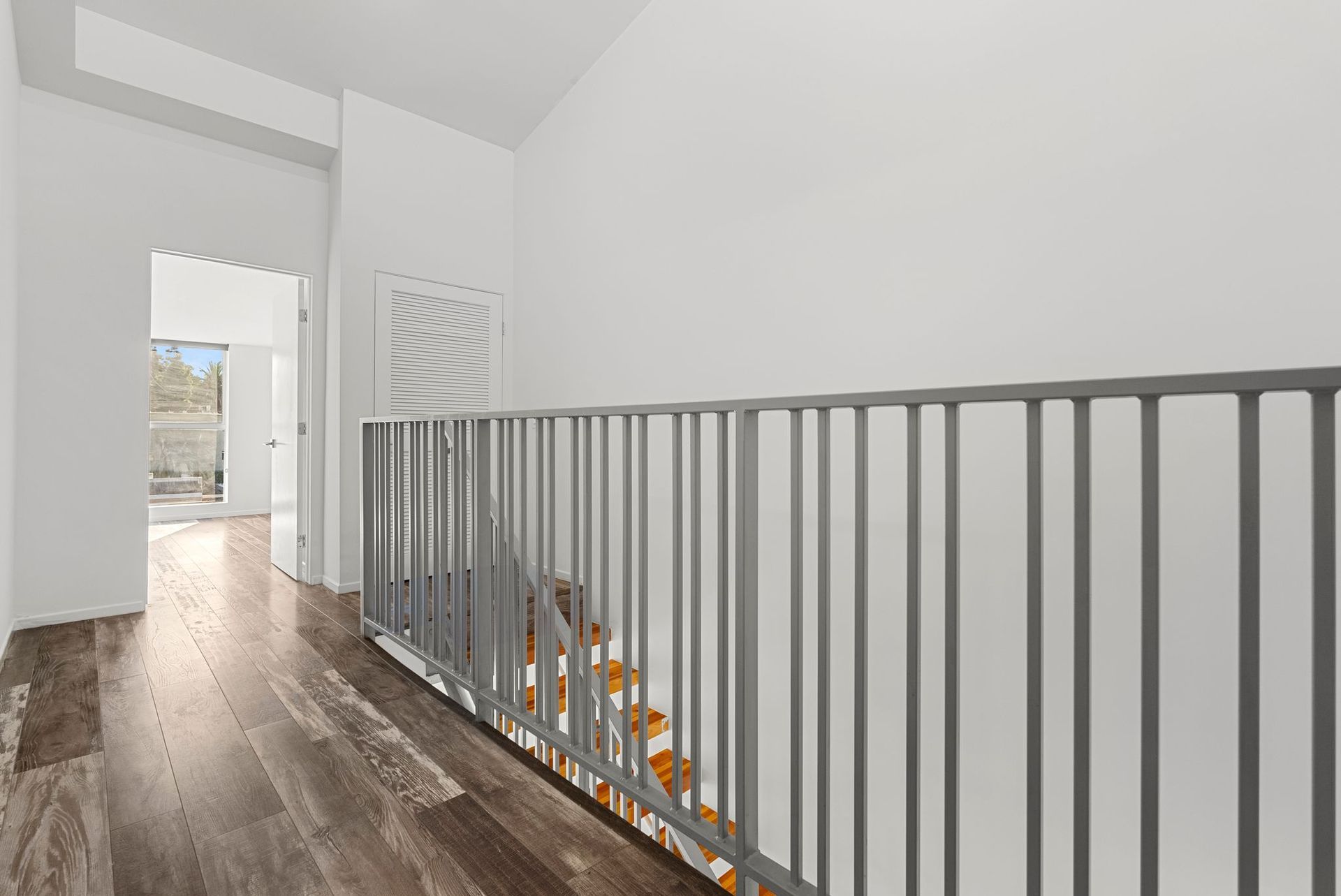 Hallway with wooden floor, stairs, metal railing, and white walls.
