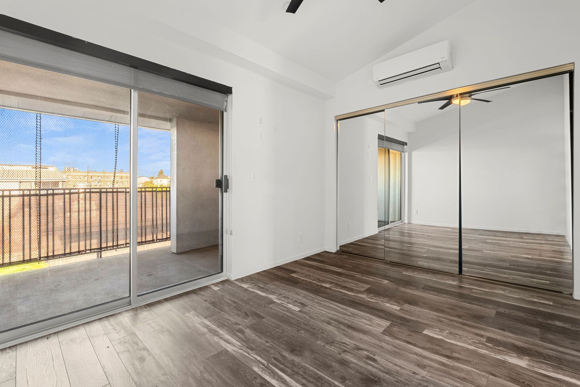 Empty room with a large mirrored closet, sliding glass door, and wooden floor.